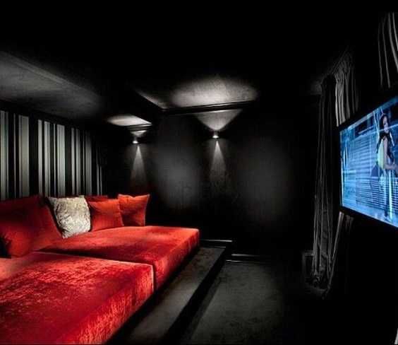 Домашний кинотеатр с ярко красным диваном и чёрными стенами и потолком